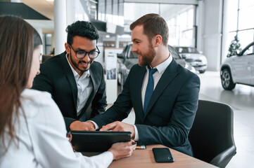Two men are buying automobile. Three people are working together in the car showroom