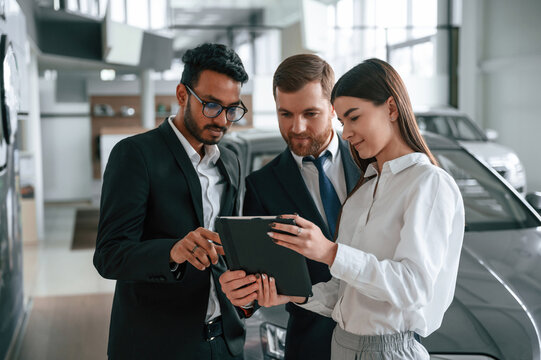 Standing and reading information in the graphic tablet. Three people are working together in the car showroom - Powered by Adobe