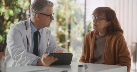 Middle Aged Physician Talking with a Senior Woman During Consultation in Health Clinic and Showing Her CT Scans on Tablet Computer. Doctor in White Coat Suggesting Treatment to Elderly Patient