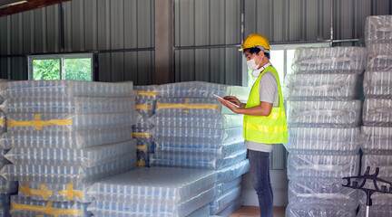Asian man worker checking the stock of plastic bottles in the warehouse and comparing the balancing number in the system after delivery shipment. Using a tablet to update online stock 