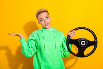 Portrait of clueless girl hand hold wheel shrug shoulders isolated on yellow color background - obrazy, fototapety, plakaty