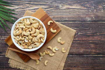 Fototapeta premium Cashew nuts in white bowl on wood table - Top view with copy space