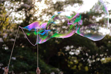 Close up a man making huge rope soap bubbles in a park