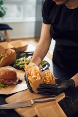 Holding French fries. Man is packing food into the paper eco boxes. Indoors, restaurant
