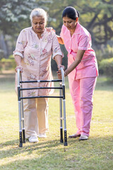 Female nurse helping senior woman with mobility walker at nursing home garden.