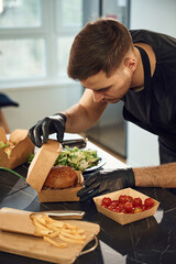 Tasty burger. Man is packing food into the paper eco boxes. Indoors, restaurant