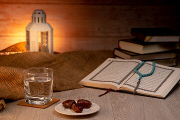 Many Date Palms are on bowls, plates, and a cup of water and the Quran Islamic style lamp on the wooden tables, to wait for the time of Iftar, with the concept of fruits from Muslims around the world.
