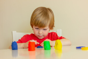 little blond boy playing with plasticine while sitting at table