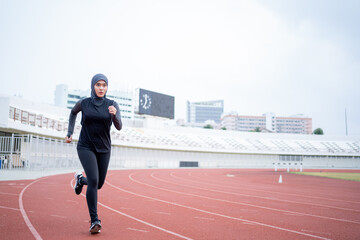 A young asian Muslim woman wearing a black hijab is exercising and running at an outdoor stadium in...