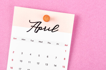 A April 2023 calendar and wooden push pin on pink colour background.