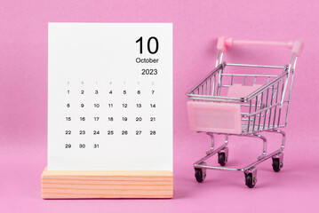 The October 2023 Monthly calendar with shopping cart against pink background.