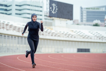 A young asian Muslim woman wearing a black hijab is exercising and running at an outdoor stadium in...