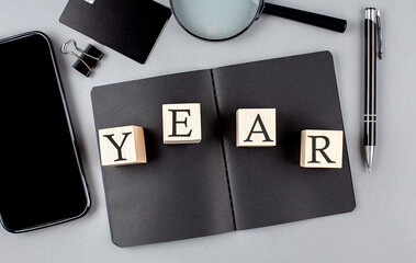 Word YEAR on wooden block on black notebook with smartpone, credit card and magnifier