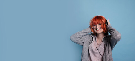 Portrait of stylish cheerful teenage girl with makeup in headphones on blue background.Large banner with negative space.