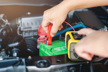 Car service and basic check concept, Technician is using charge charger meter to check battery voltage in engine room and push switch to charger battery and vehicle electrical system basic inspection