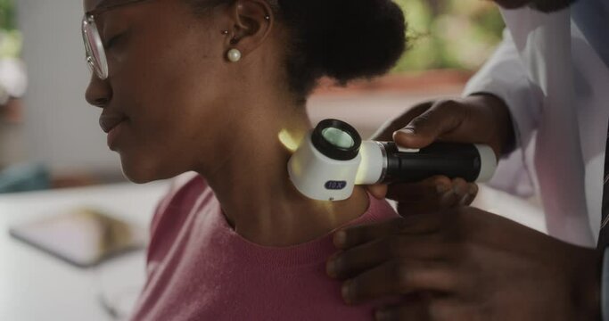 Close Up Footage of an African Skin Care Professional Using a Dermatoscope to Examine Neck Tissue on the Skin of a Young Black Female During a Health Check Visit to a Clinic. Dermatologist in Hospital