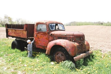 young child with piqued curiosity about an old rusty truck in a famers field