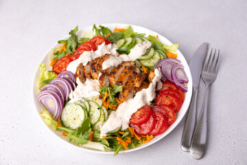 Warm salad with chicken, arugula, fresh vegetables and sour cream (yogurt) sauce. Home cooking, healthy food. White background, selective focus, close-up.