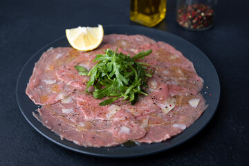 Marbled beef carpaccio with arugula, parmesan cheese, olive oil and lemon. A traditional classic appetizer made from thinly sliced raw meat. Close-up, selective focus, black background.