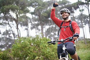 This feels great. A young male athlete pumping his fist in the air after conquering a mountain biking trail.