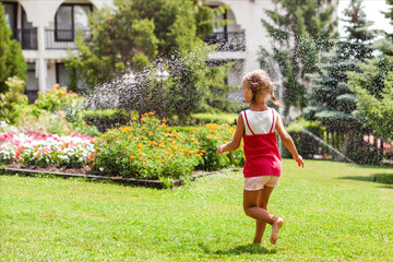 Happy Child Having fun Running with Water Spray in Garden. Funny little Girl playing with Garden Sprinkler in sunny Nature. Summer Outdoors Activity for Kids. - obrazy, fototapety, plakaty