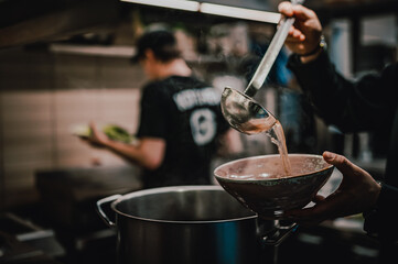 chef pouring tasty soup from big pot into bowl on restaurant kitchen