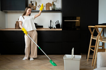 Carefree happy woman cleaning the living room at home is dancing merrily with a mop