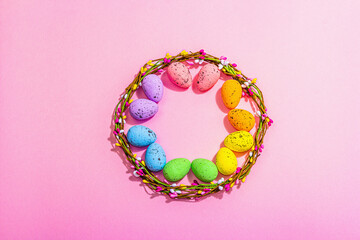 Easter wreath with colorful eggs on pink background. Artificial floral decor, festive symbols