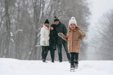 Girl is standing in front of his parents and brother. Happy family is outdoors, enjoying snow time at winter together