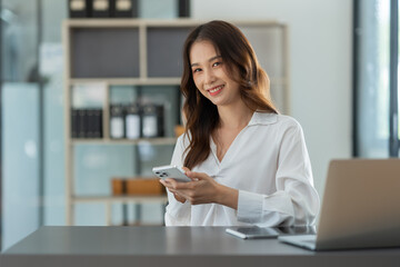 Beautiful Asian businesswoman working on a laptop computer using a mobile phone to negotiate financial business accounting analysis, report, and office information.