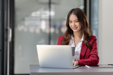 Fototapeta na wymiar Beautiful Asian businesswoman holding a cup of coffee relax Take breaks and work hard on financial business matters at the office and have fun. Smiling happy working with the laptop.