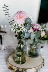 Tischdeko mit weißer Tischdecke und Blumenvasen auf Holzscheiben bei Hochzeit
