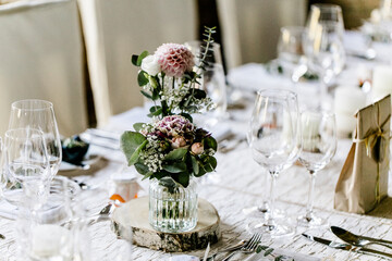 Tischdeko mit weißer Tischdecke und Blumenvasen auf Holzscheiben bei Hochzeit