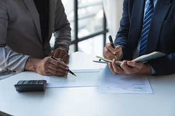 Two young Asian businessmen analyzing Calculate and discuss and brainstorm data, charts, graphs Taking notes on financial reports in notebooks at office financial advisors and accounting concepts.