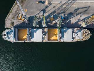 Aerial view of a bulk carrier ship loaded with grain is docked at a busy port, with workers and...