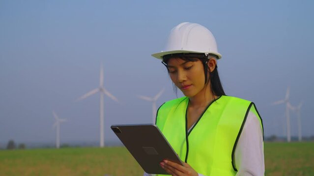 Female engineer checking and survay wind turbine location. She using tablet to check data and work.