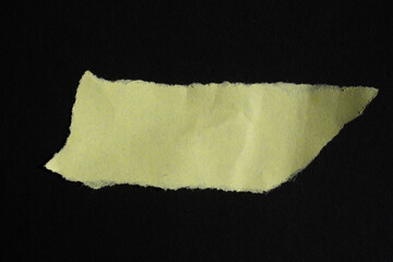 Yellow torn paper piece isolated on a black background. Ripped blank paper with copy space for text.
