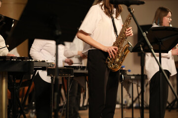 A group of students in a school orchestra play jazz on different musical instruments golden saxophone in a female hand close up