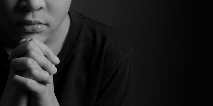 boy praying to God with hands held together with closed eyes on grey black background stock photo	
