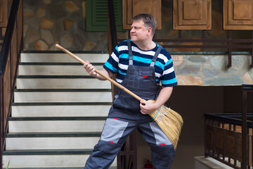 A worker with a broom dances imitating a rock star near the house.