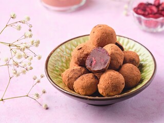 Homemade chocolate truffles with dried cherries in a ceramic bowl on a pink concrete background.