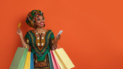 Dreamy african woman shopaholic holding phone and bank card