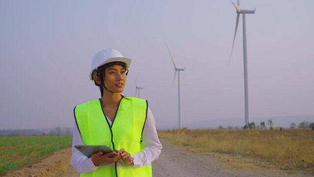 Female engineer checking and survay wind turbine location. She using tablet to check data and work.
