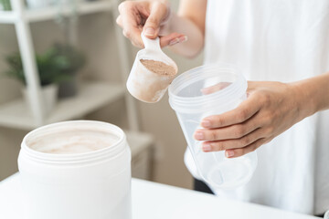 Obraz na płótnie Canvas Young sporty woman pouring protein powder into a cup to make replacement food meal after workout