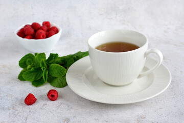 A cup of tea with a bowl of raspberries and green leaf of mint on the marble table