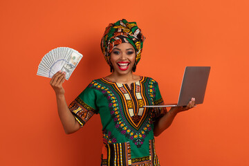 Obraz premium Rich african woman holding cash and pc laptop