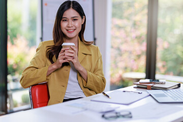 Obraz premium Concept of business office woman working,Businesswoman smile while working about her invesment plan with analyzing document and business investment graph data and holding coffee cup in workstation