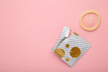 Opened condom in pack on pink background. A condom use to reduce the probability of pregnancy or...