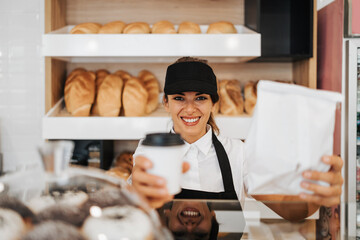 Fototapeta na wymiar Beautiful young and happy female worker working in a modern bakery or fast food restaurant.
