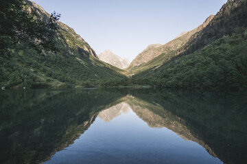 Morning landscape in the mountains with a lake in a valley between mountain slopes and rocks with a forest, a mirror surface of a mountain lake in the morning